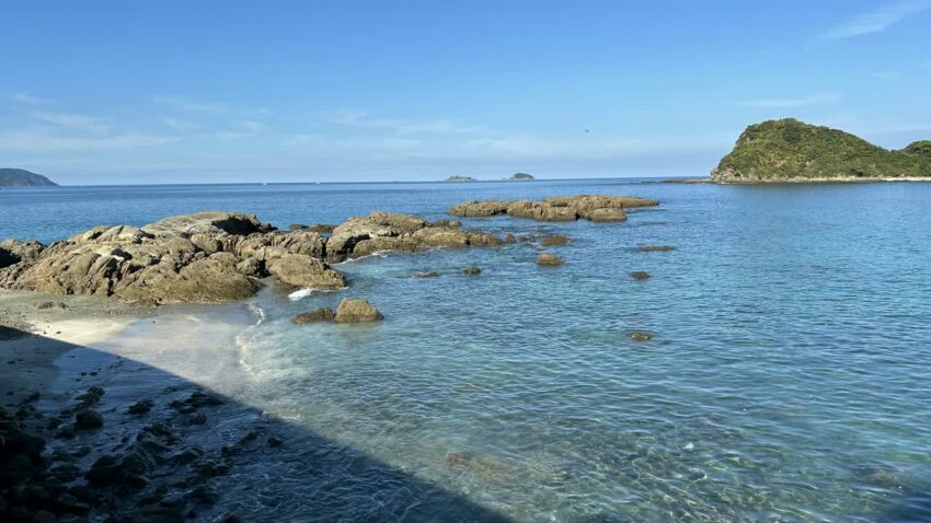 くじら浜から見た岩場と浅瀬、沖の緑に覆われた島